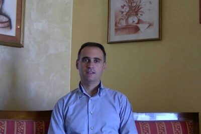 Professional-looking man seated on a patterned bench in a warm interior representing la giurisprudenza.