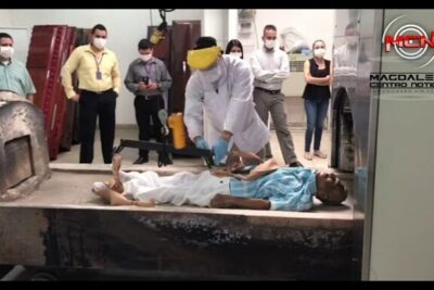 Technician in protective gear preparing a body for la incineracion inside a crematorium room with observers