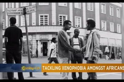 Black-and-white street scene of men shaking hands and speaking in a public square about la xenophobie.