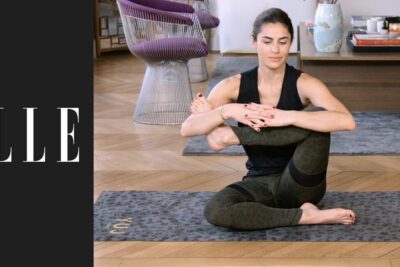 Woman practicing le yoga 1 seated leg-hug stretch on a patterned mat in a bright living room