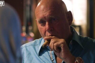 Bald man holding a cigar in a dim bar looking thoughtful while reflecting on legalisation prostitution