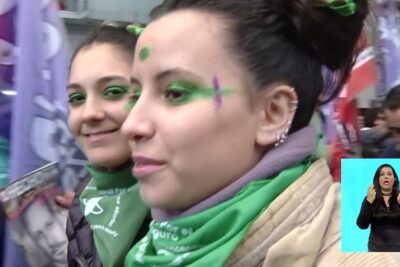 Two young women at a crowded street protest wearing green bandanas and face paint advocating legalizacao aborto 1