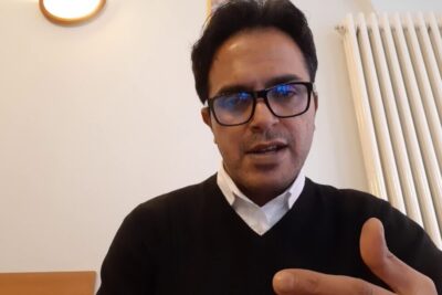 Person wearing glasses and a dark sweater gesturing while speaking about legge italiana