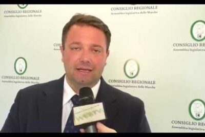 Man in suit being interviewed with a microphone in front of a regional council backdrop for legge tabacco coverage.