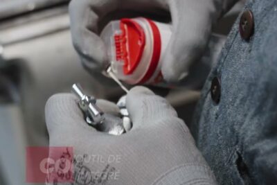 Gloved hands applying letancheite filetages sealant to a metal threaded fitting