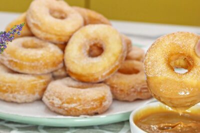 Hand holding a sugar-coated donut being dipped into caramel sauce, leva bilden