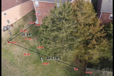Aerial view of a backyard showing black measurement lines, red distance markers and a large tree, leve image