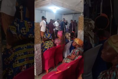 Indoor community choir performance in a small hall with seated audience wearing colorful headwraps, lexistence destinee