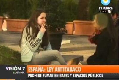 Two people seated outdoors, one smoking, with a television news banner referencing ley antitabaco 1.