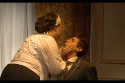 Woman leaning in and holding a seated man's face in a dramatic stage moment libero scambio 1.