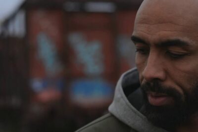 Close-up contemplative portrait of a bearded man against a blurred graffiti background, libertad expresion 2