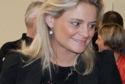 Smiling blonde woman at an indoor gathering, illustrative for ligestilling i aegteskab for og imod homoseksuelle aegteskaber.