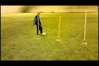 Young player dribbling a soccer ball through slalom poles on indoor turf lisaksi jalkapallo