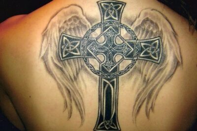 Detailed back tattoo of a Celtic cross framed by angel wings, los tatuajes 3.