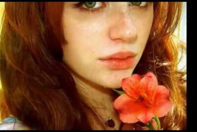 Close-up portrait of a red-haired person holding a coral flower, maggiore eta 1