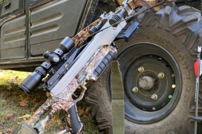 Camo crossbow leaning against an ATV tire with arrows and magt styring