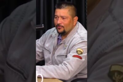Man in a gray jacket speaking into a microphone at a table, portrait-style image referencing maioridade 16.