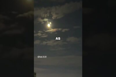 Night sky with a bright moon and secondary flare resembling a manen planet above scattered clouds.
