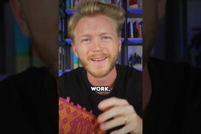 Smiling presenter holding a patterned notebook in front of a bookshelf, suitable for marx ideer visuals