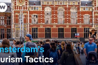Crowded group of visitors outside the historic Amsterdam Centraal station illustrating mass tourism 1.