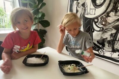 Two children doing sensory crafts at a table with bowls and wooden sticks, minedrift danmark.