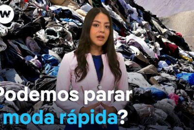 Television presenter standing before a mountain of discarded garments illustrating moda rapida impact.
