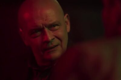 Close-up of a bald man in red-lit interior with a contemplative expression, moderat alkoholforbrug 1