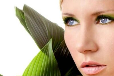 Close-up of a woman's face with green eye makeup and large leaves, featuring monsanton tuotteiden 1