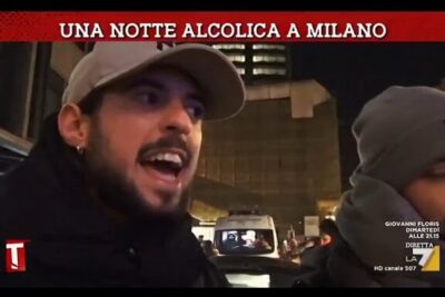Two men speaking on a Milan street at night beneath a banner referencing movida alcolica