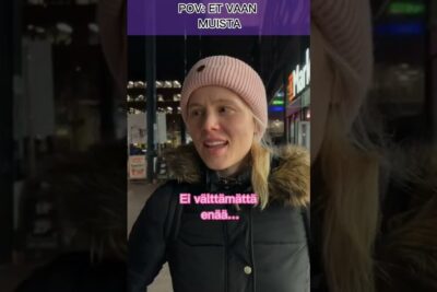 Woman wearing a pink beanie and fur-trimmed winter coat on a city sidewalk at night, muista elaimista.