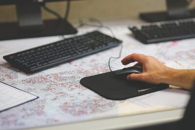 Hand using a computer mouse on a desk with keyboard and planning documents, workspace for negocios