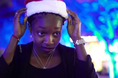 Woman adjusting a Santa hat amid blue holiday lights at a noel fete