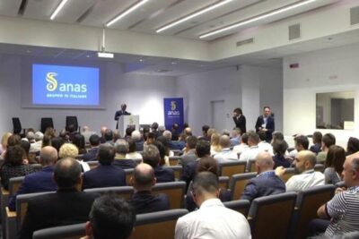 Crowded conference room with a speaker and audience focused on norme internazionali and global standards
