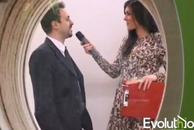 Woman interviewer holding a microphone to a suited man in front of a circular display, capturing a discussion about numerosi vantaggi.