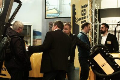 Attendees discussing yellow industrial machinery at a trade show showcasing nya produkter.