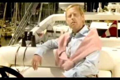 Man seated on a yacht deck at a marina with docked boats and masts, offentlig transport