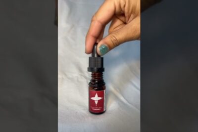 Amber glass dropper bottle with red label and a hand removing the black cap, okologiske produkter 1.