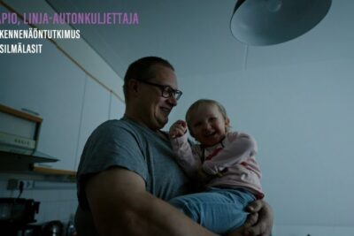 Adult male wearing glasses holding a smiling toddler in a softly lit kitchen, on tarkeaa 79