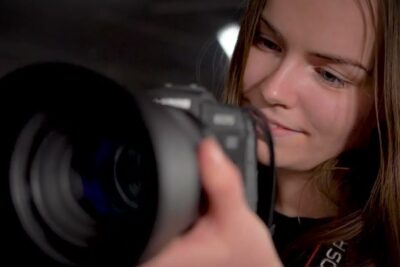 Woman inspecting a DSLR camera lens up close on tarkeaa 92