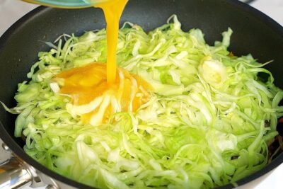 Shredded cabbage in a frying pan with an egg being poured to opretholde sund