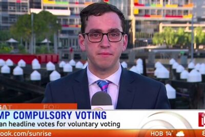 TV reporter delivering a live segment about optional voting 1 and dumping compulsory voting at a waterfront location.
