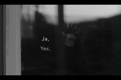 Black and white photo of a window reflection showing the words 'Ja, Yes' and smudged glass, pa jorden 13