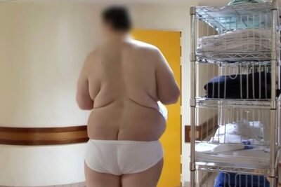 Back view of a person in white underwear standing beside metal shelving with towels, pa utseende visible