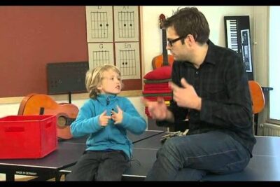 A child and an adult engaging in a music lesson with guitars and chord charts in view pa verkligheten 1.