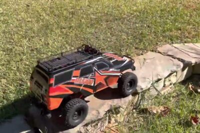Orange and black RC van pa vindresa climbing stone edging in a sunny grassy yard.