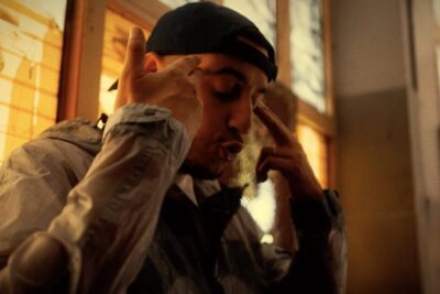 Man in a backward cap and lightweight jacket making expressive hand gestures near his temples in warm window light, labeled peine mort 5