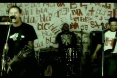 Three-member punk rock band performing in a graffiti-covered room with a raw pena perpetua aesthetic