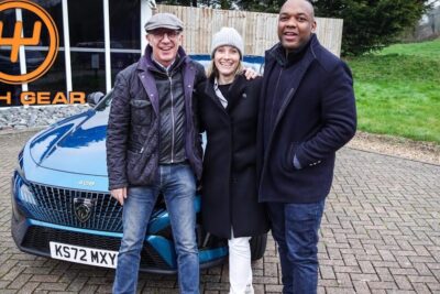 Three people posing beside a blue peugeot 408 10 parked outside a garage