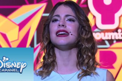 Female vocalist on a colorful stage with a headset microphone and Disney Channel logo, podemos