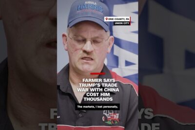 Close-up of a farmer wearing a cap and glasses speaking in front of a news headline about a trade war and politisk union discussions